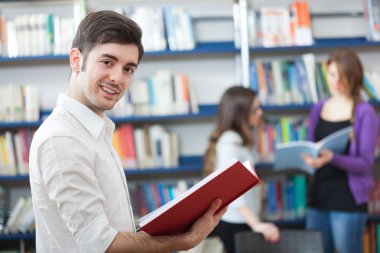 Genç adam bir kitaplıktaki bir kitap okuma