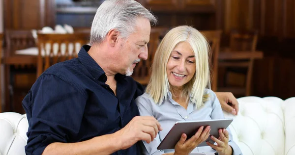 Gülümseyen Bir Olgun Çift Dijital Tablet Kanepe Evde Kullanma Portresi — Stok fotoğraf