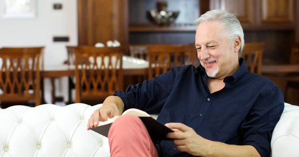 Ώριμος Άνδρας Χαλάρωσης Διαβάζοντας Ένα Βιβλίο Ένα Καναπέ Στο Σπίτι — Φωτογραφία Αρχείου