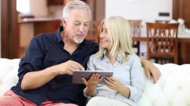 Gülümseyen bir Olgun çift dijital tablet kanepe ev 4 k kullanma portresi