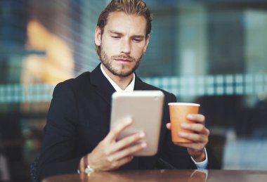 Bir fincan kahve zevk ve onun tablet seyir yakışıklı işadamı