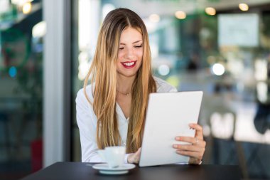 Kahve molasında olan genç iş kadını tablet bilgisayar kullanıyor.