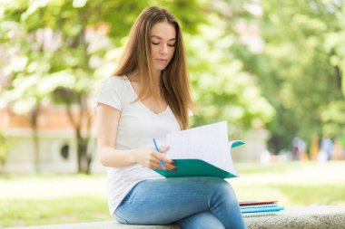 Güzel bir üniversite öğrencisi parkta bir bankta kitap okuyor.