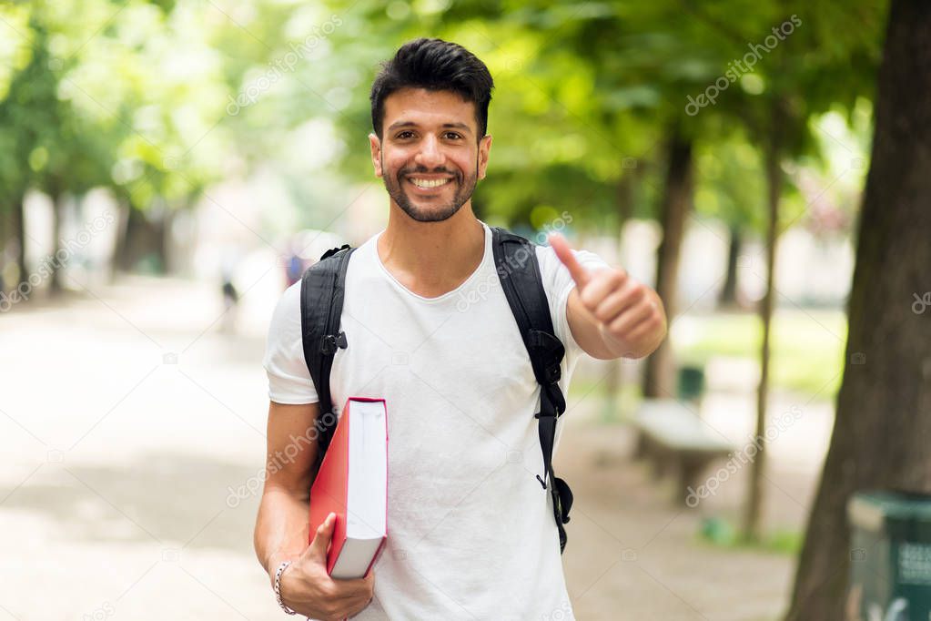 Smiling student holding book, showing thumb up 