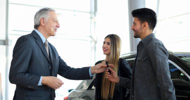 Güzel genç sahipleri için yeni araba anahtarını vererek araba satıcısı