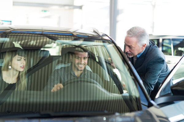 Счастливая молодая семья разговаривает с продавцом и выбирает свой новый автомобиль в автосалоне