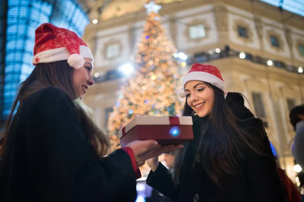 Young smiling women in Christmas hat exchanging presents