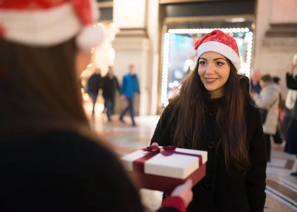 Young smiling women in Christmas hats exchanging presents