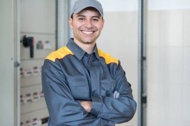 Bir fabrikada bir endüstriyel elektrik paneli önünde gülümseyen bir elektrikçi portresi