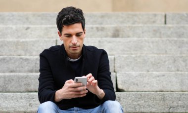 Açık merdivenlerde oturan bir akıllı telefon kullanan genç adam