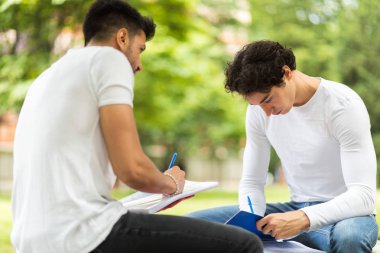 İki öğrenci açık hava bankında birlikte ders çalışıyor.