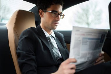 Bir arabanın arka koltuğunda bir gazete okuyor genç Yöneticisi