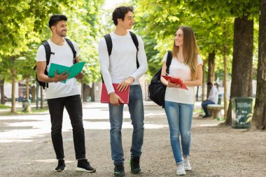 Üniversite bahçesinde birbirleriyle konuşan üç öğrenci.