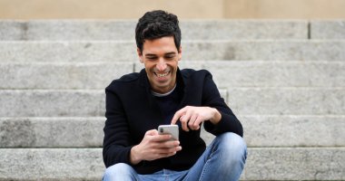 Açık merdivenlerde oturan bir akıllı telefon kullanan genç adam