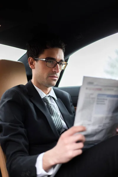 Young manager reading a newspaper in the back seat of a car