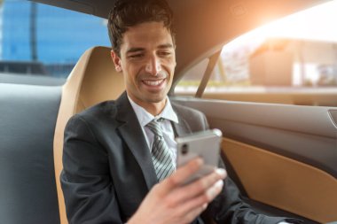 Bir arabanın arka koltuğunda cep telefonunu kullanan işadamı