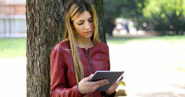 Genç kadın bir ağaç parkta karşı yalan ve kablosuz internet bağlantısı özgürlüğü zevk dijital tablet kullanma