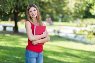 Güzel bir kız öğrenci açık havada kitap tutuyor.