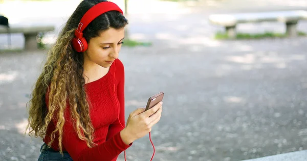 Woman listening to music sitting on bench in a park