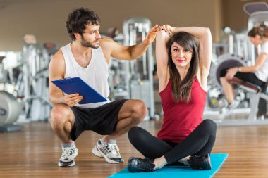 Kadının bir kişisel antrenör onu izlerken bir spor salonunda germe yapması
