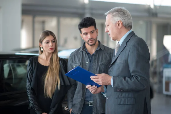 Happy young family talking to the salesman in a car showroom