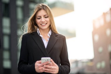 Gülümseyen iş kadını cep telefonunu kullanıyor.