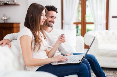 Mutlu çift kanepede bir dizüstü bilgisayar kullanarak