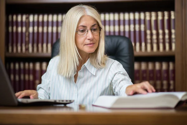 Mogen Kvinna Som Använder Sin Bärbara Dator Medan Läser Bok — Stockfoto