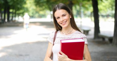 Parkta kitap tutan gülümseyen öğrenci 