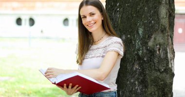 Parkta gülümseyen öğrenci okuma kitabı 