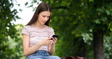 Genç kadın parkta bir bankta akıllı telefon kullanıyor