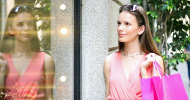 Güzel genç kadın alışveriş çantası tutan ve vitrin bakarak