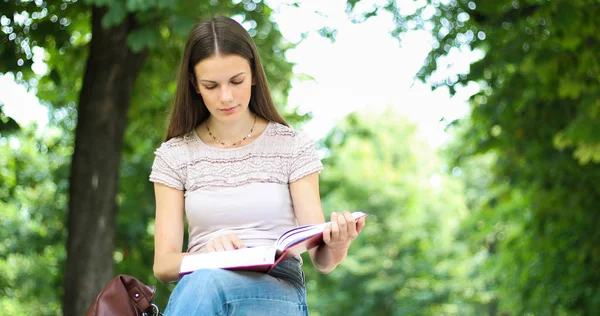 美丽的女大学生在公园的长椅上看书 — 图库照片