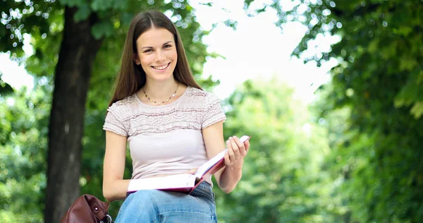 美丽的女大学生在公园的长椅上看书 — 图库照片