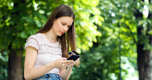 Portrait of a happy woman paying online with credit card and smartphone in a park