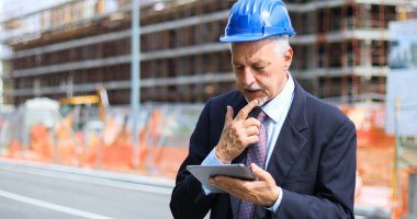 Kıdemli mühendis erkek takım elbise ve tablet PC'de çalışma kask