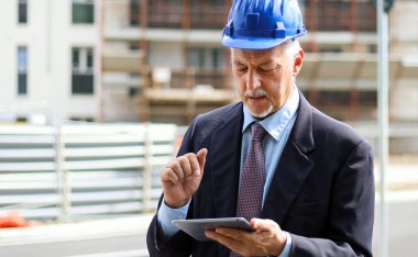 Kıdemli mühendis erkek takım elbise ve tablet PC'de çalışma kask