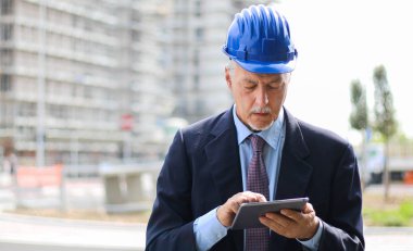 Kıdemli mühendis erkek takım elbise ve tablet PC'de çalışma kask