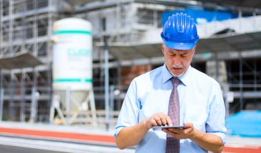 Kıdemli mühendis erkek takım elbise ve tablet PC'de çalışma kask