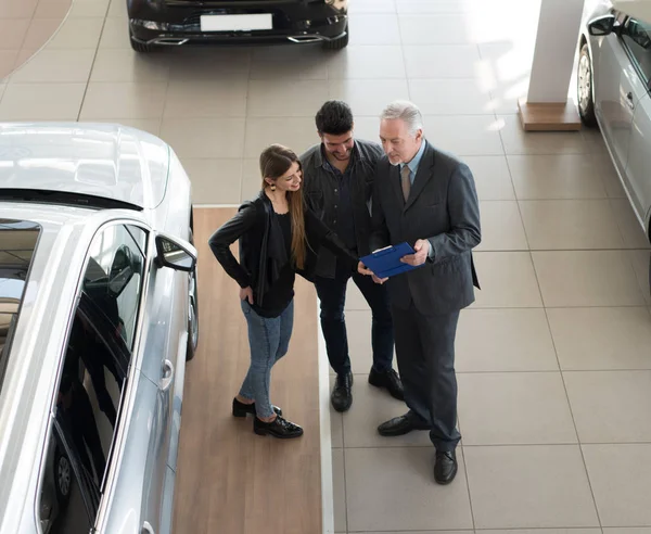 Jovem Família Conversando Com Vendedor Escolhendo Seu Novo Carro Showroom — Fotografia de Stock