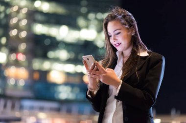 Akşamları modern bir şehirde akıllı telefonunu kullanan bir kadın.