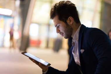 Genç yönetici, modern bir şehirde geceleri dijital tablet kullanıyor.