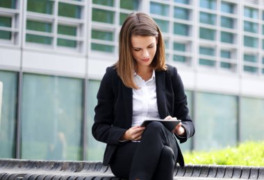 Dijital tablet kullanan gülümseyen iş kadını bankta oturuyor.