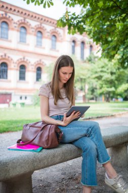 Parkta dijital tablet kullanan gülümseyen bir kadının portresi.