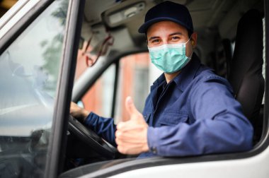 Minibüs şoförünün portresi başparmak işareti yapıyor ve maske takıyor. Coronavirus konsepti.
