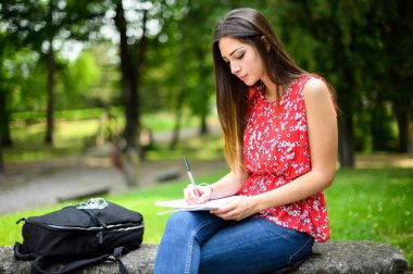 Güzel bir üniversite öğrencisi parkta bir bankta kitap okuyor.