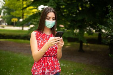 Cep telefonunu kullanan maskeli genç bir kadın.