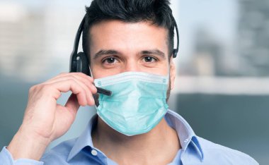 Maskeli adam mikrofon kulaklığını uzaktan arama için kullanıyor.