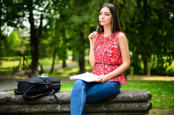 Güzel bir üniversite öğrencisi parkta bir bankta kitap okuyor.