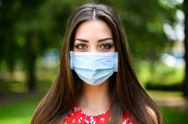 Coronavirus zamanlarında parkta maske takan güzel bir kadının portresi.
